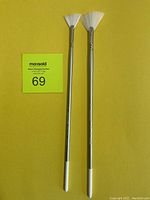 Two new Silverwhite fan paint brushes against a yellow background, showing full brushes including handles and bristles.