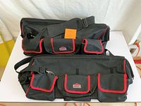 Two black Jobmate tool bags side by side showing multiple external pockets with red trim, top carry handles, and shoulder strap on each.