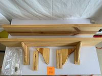 Two unfinished pine wood shelves lying flat with four wooden mounting brackets and a bag of screws and mounting hardware beside them.