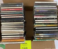 Two stacks of various pop and rock CD jewel cases showing album titles and artists.