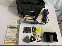 Rockwell SoniCrafter multitool with accessories, user manual, carrying bag and accessory box arranged neatly including sanding pads, cutting blades, hex keys and sanding pads.