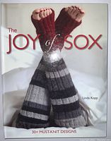 Cover of The Joy of Sox book showing a pair of grey and black striped knit socks worn by a person lying down.