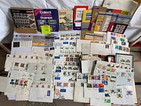 Wide view of stamp collection contents including reference books, first day covers, albums, and loose stamps spread out