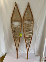 Full view of pair of vintage Ojibwe style wooden snowshoes with woven rawhide webbing and leather bindings.