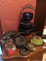 Overview of cast iron teapots, ceramic saucers, manual grinder, and plate rack with stacked plates