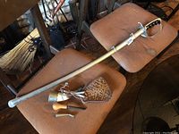 Full view of the 30-inch ceremonial sabre lying on a chair, showing metal scabbard and curved hand guard.