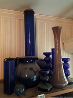 Full view of assorted cobalt blue glass bottles and vases showing the tallest vase at 22.5 inches plus other varied shapes including bulbous forms and one mauve glass vase.