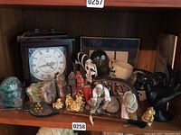 Wide view showing the wooden Wallace Quartz clock with Roman numeral face surrounded by multiple collectible figurines and minerals on a wooden shelf.