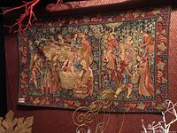 Full view of the tapestry hung on wall showing the entire woven medieval scene with multiple figures and decorative border.