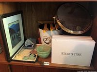 Shelf with Lalique box containing blue crystal fish, framed artwork, vintage lace and fabric bows, and other small items.