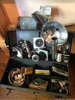 Overview of open metal case with assorted lenses, flash reflectors, bulbs, film holders and accessories