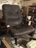 Front angled view of mid-century modern lounge chair in dark brown leather with visible wear and wooden armrests and swivel base.