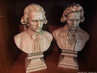 Front view showing both busts of Mozart and Beethoven displayed side-by-side on a wooden shelf.