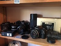 Shelf view showing three Nikon SLR cameras with lenses, Braun flash and Nikon TV box