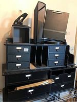 Photo of black metal and plastic office organizers with multiple drawers and compartments stacked on a metal rack.