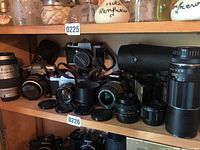 Top shelf display of four cameras, lenses, flash and accessories under lot label 0225