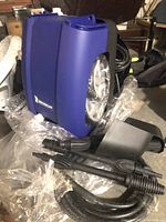 Blue Michelin MPX1450 power washer with attached coil of black hose and spray wand attachments laid beside it on table.