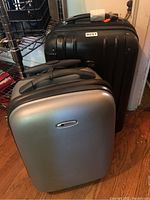 Two carry-on suitcases, one silver Delsey hard shell in front and one black suitcase behind it