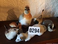 Photo of seven USSR Soviet porcelain miniature figurines placed on a wooden surface including various birds and animals under indoor lighting.