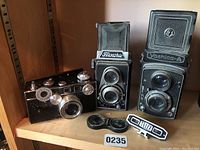 Overview photo showing the Argus 'Brick', Flexora TLR, Yashica-A TLR cameras and Telex rangefinder accessory arranged on a shelf.