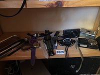 Overview of watches and digital cameras arranged on a wooden shelf, showing variety of wristwatches in front and digital cameras at the back