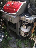 Front view of grill with lid closed, side table folded down, mounted propane tank on lower shelf