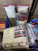 Photo showing two plastic bags of white curtains, rolled tropical towel, packaged lace curtains, floral linens, and flannel sheet set