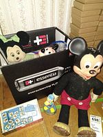 Box on the floor with Minnie Mouse plush, Donald Duck figure, Mickey Mouse doll inside, large Marching Mickey Mouse doll standing outside box, Disney domino set visible