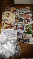 Photo of multiple doll books, magazines, and ephemera spread on wood floor including a plastic bag with packing materials.