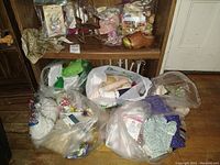 Photo of bags with vintage doll clothes and fabric, doll parts inside plastic bags, and wooden doll rocking chair on shelf.