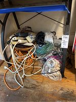 View of multiple extension cords in different colors coiled and some packed in plastic bags, along with a battery charger unit under a table.