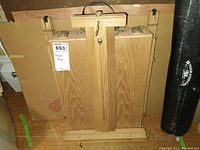 Top view of wooden portable easel case with metal clasps and handle, packed with sketching materials inside.