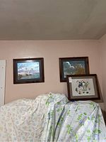 View of three framed prints hung on a wall above covered furniture. Two prints depict birds and nature scenes, one smaller print is propped against the wall.