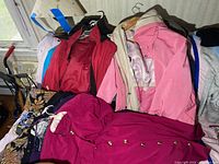 Lot of jackets and outerwear on hangers including red, pink, cream, and patterned jackets packed together.