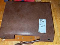Brown rectangular carrying case with a broken strap showing metal details on a wooden surface.