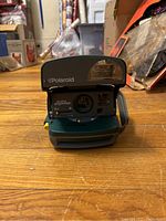 Front view of the Polaroid One Step Express camera showing lens, flash, and brand markings on wood floor.