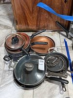 Overview of pots and pans showing multiple copper-colored cookware pieces with black handles and glass lids stacked together.
