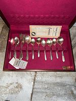 Opened flatware box revealing ten pieces of Tudor Plate silverplate flatware including spoons and forks, arranged in individual slots within a burgundy velvet-like lining.