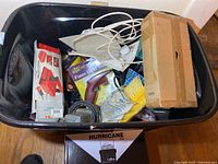 Black plastic tote filled with tools including boxed Mighty Car Vac handheld vacuum, cords, LightKeeper Fixes Light Sets kit, and cardboard box.