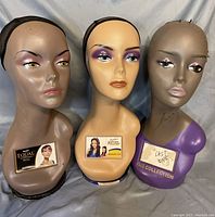 Front view of three long neck wig heads showing painted makeup and brand tags