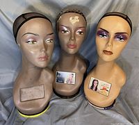 Front view of three long neck wig heads with mesh caps, one head with damage mark on the forehead.