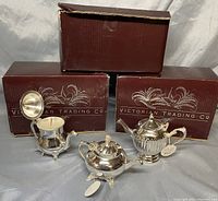 Three silverplate teapot-shaped scented candles displayed with three original Victorian Trading Company boxes in background.