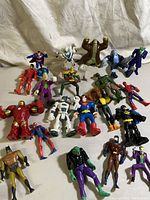 Assorted superheroes and villains action figures displayed on white fabric background; includes Superman, Batman variants, Joker, Iron Man, Spider-Man, and others.