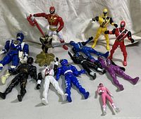 Photo showing 12 Power Rangers action figures in various poses and colors including red, blue, yellow, pink, purple, black, white, and gold accented figures.