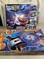 Photo showing both the Beyblade Burst Surge Motor Strike Battle Set box and Head 2 Head Space Wars pinball game box side by side on a table.