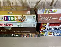 Stack of various boxed board games including The Game of Life, Monopoly, Trivial Pursuit, Clue, and The Beer Game.