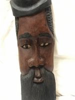 Front view of the large wooden mask showing the face with beard and beret hat.