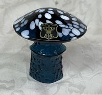 Close-up of the hand blown glass mushroom showing the dark cap with white spots, textured blue stem, and Golden Crown E&R Sweden gold label.