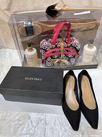 Ellen Tracy Vanilla Cassis spa set including body wash, hand and body cream, bath brush, and travel bag in clear packaging next to black shoe box and black pumps.