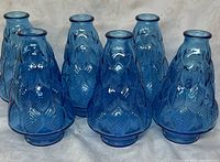 Photo showing six blue glass vases grouped together, highlighting the overlapping leaf pattern and shape.
